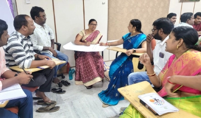 A group of educators and professionals stand in front of a government primary school during a PDC field visit for the KIX project observation.